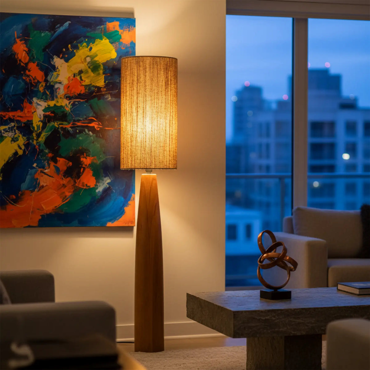Lampadaire pied bois allumé près d'un tableau abstrait coloré et d'une baie vitrée sur la ville