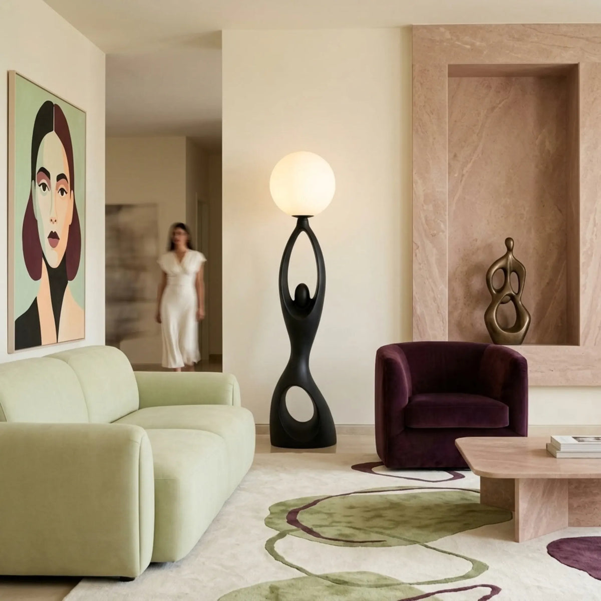 Lampadaire abstrait noir entre un canapé vert sauge et un fauteuil en velours prune