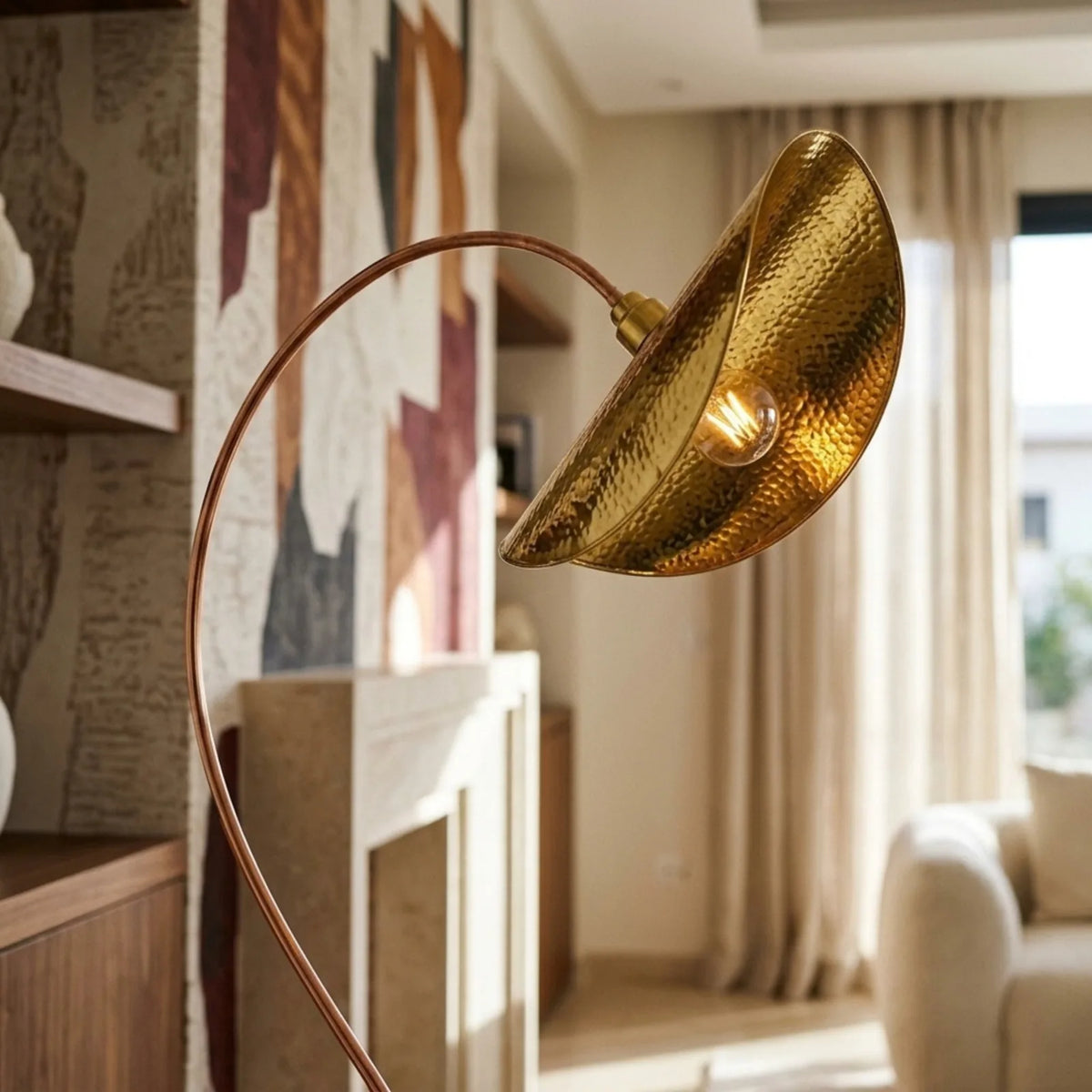 Abat-jour doré du lampadaire arc devant un mur peint aux tons terracotta, près d'un fauteuil blanc