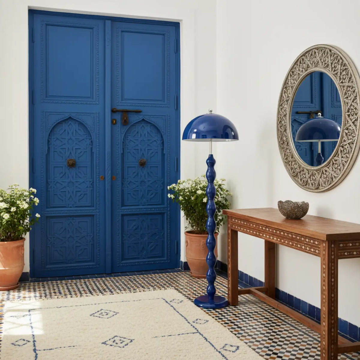 Lampadaire bleu dans une entrée avec porte bleue sculptée de style tunisien, console en bois et miroir