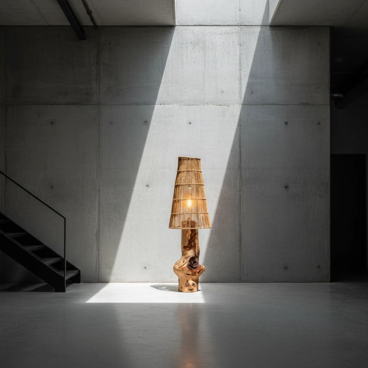 Lampadaire en bois et fibres tressées éclairé par un rai de lumière dans un espace en béton brut