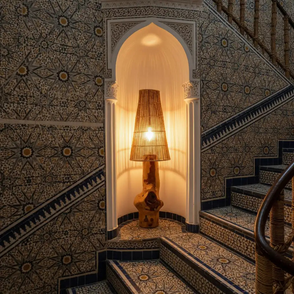 Lampadaire en bois allumé dans une niche en arc au pied d'un escalier revêtu de zellige