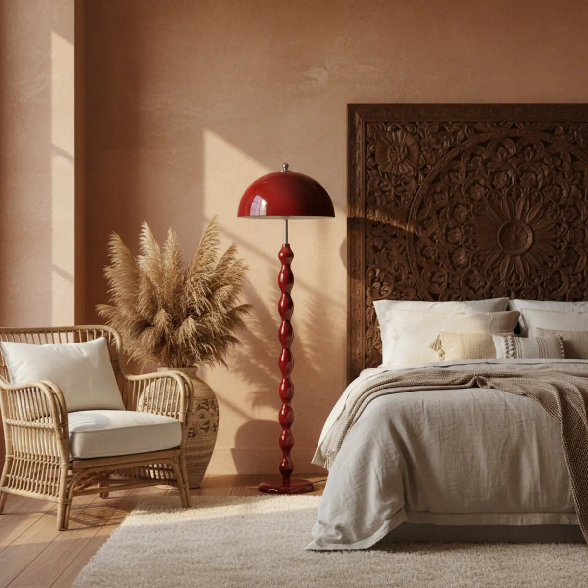 Lampadaire bordeaux dans une chambre, entre un fauteuil en rotin et une tête de lit en bois sculpté