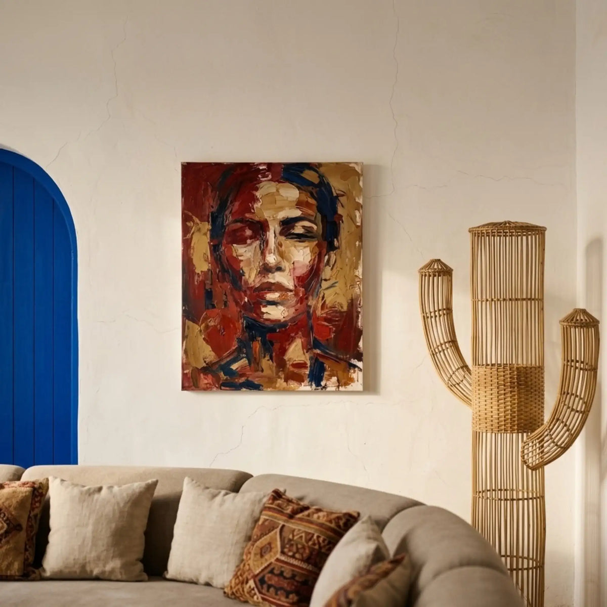 Lampadaire cactus en rotin derrière un canapé beige, à côté d'un portrait peint aux tons rouges et d'une porte bleue