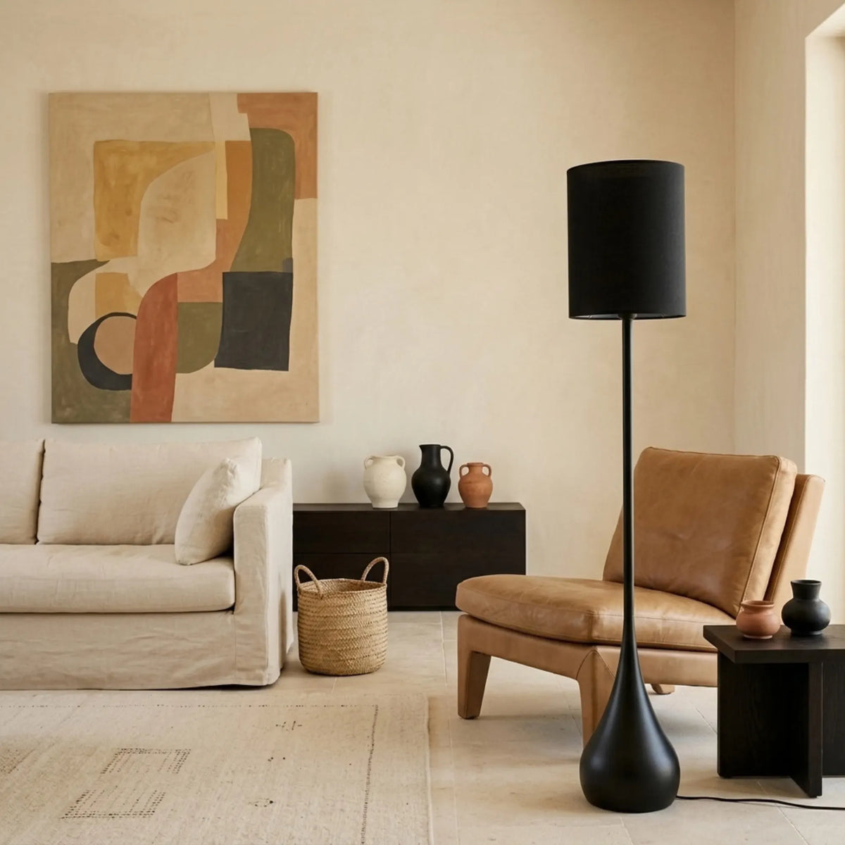 Lampadaire noir Goutte à côté d'un fauteuil camel, dans un coin lecture lumineux avec canapé crème et tableau abstrait