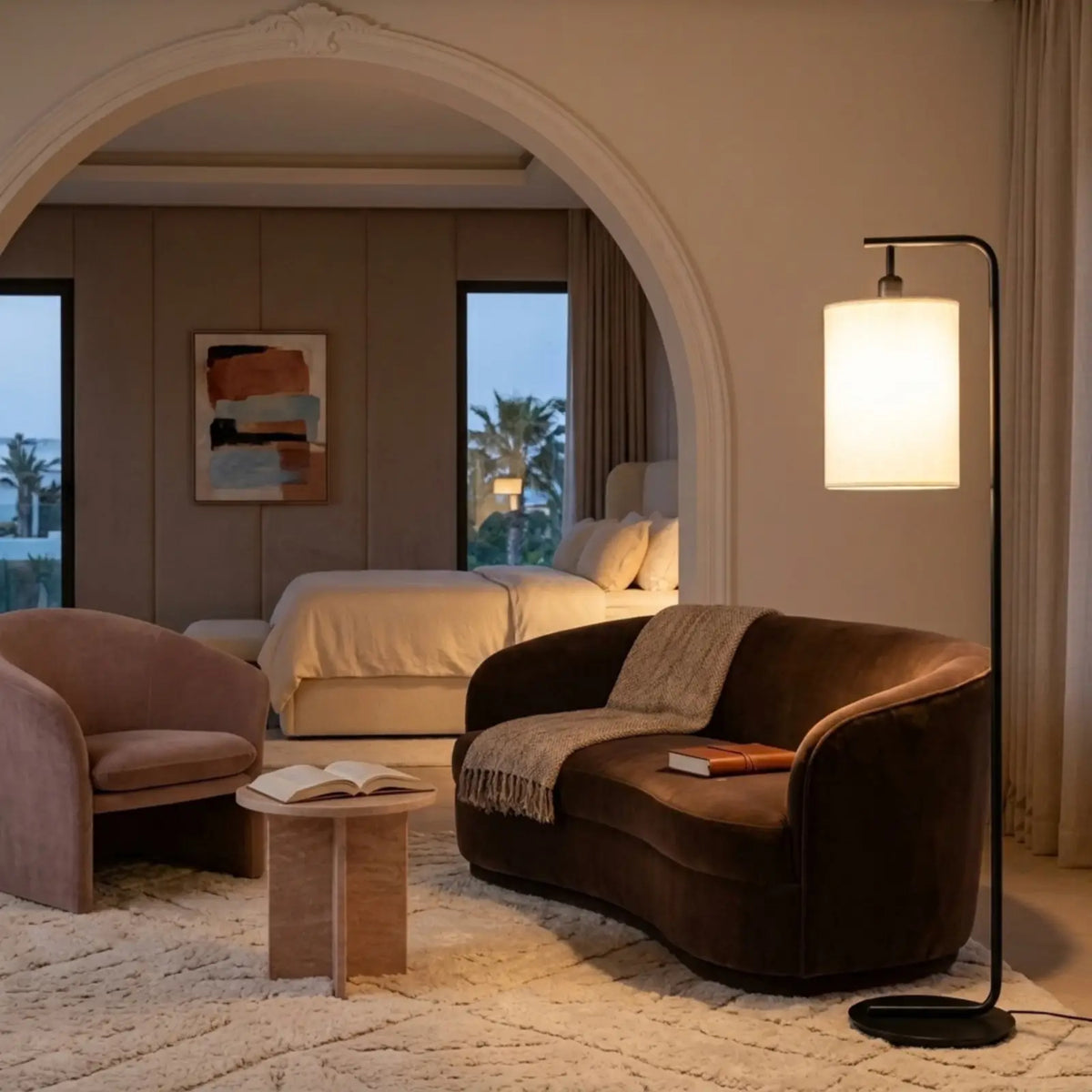 Lampadaire noir allumé près d'un canapé en velours marron, devant une arche ouvrant sur une chambre