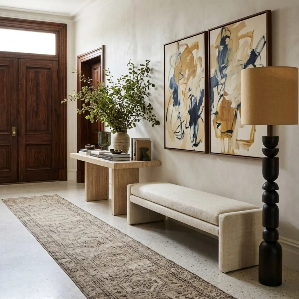 Lampadaire colonne dans un hall d'entrée, à côté d'un banc crème, d'une console et de deux tableaux abstraits