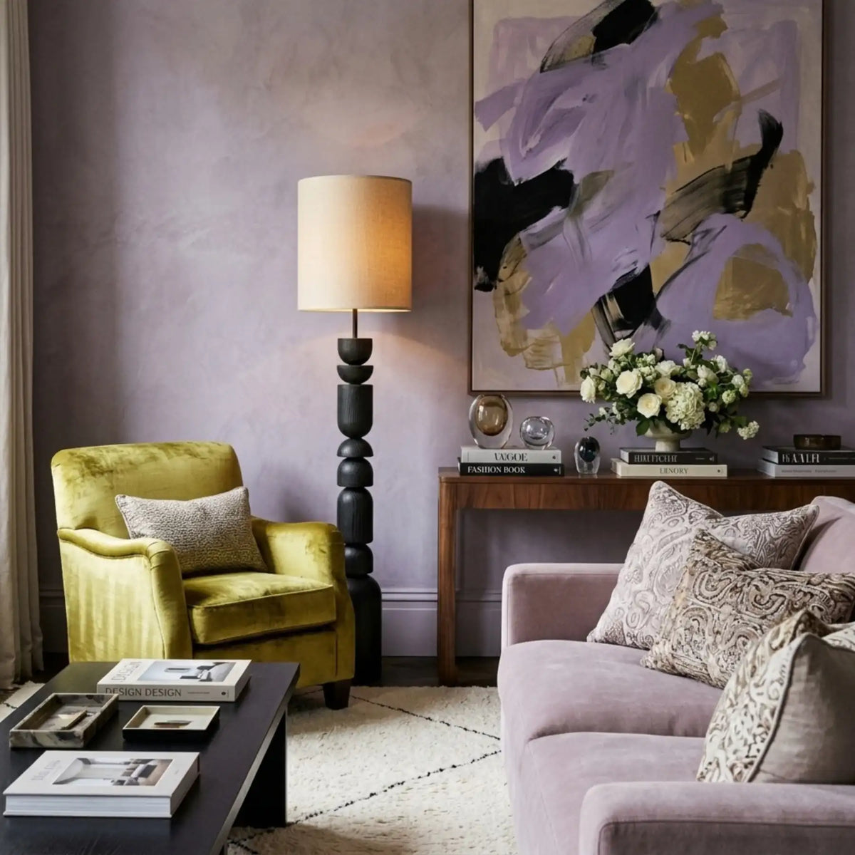 Lampadaire colonne allumé dans un salon aux murs mauves, entre un fauteuil en velours jaune et un canapé rose poudré