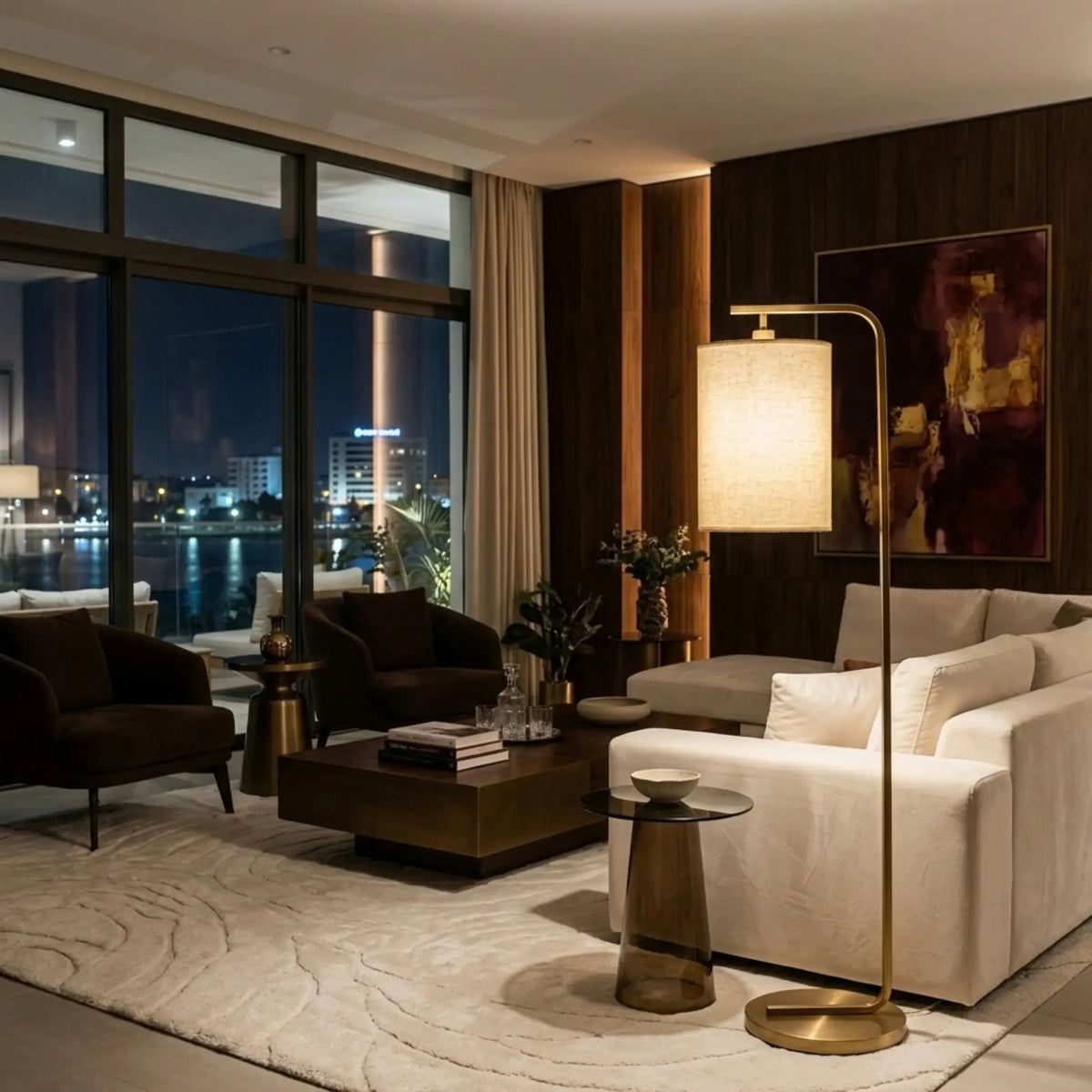 Lampadaire doré allumé près d'un canapé d'angle blanc dans un salon avec vue sur la ville de nuit