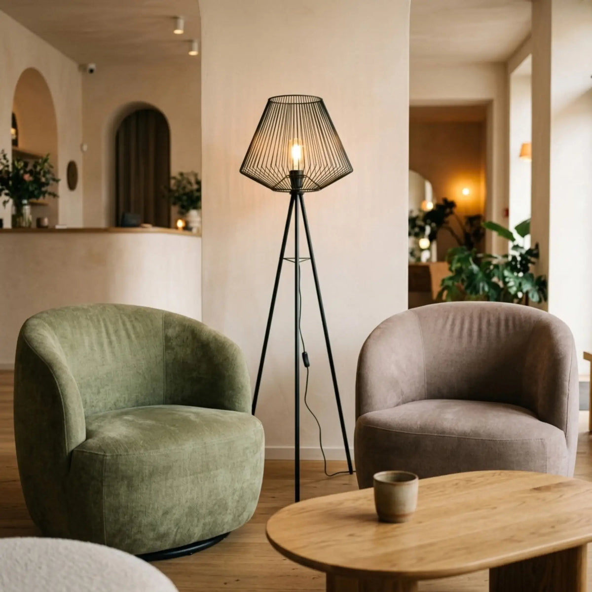 Lampadaire filaire allumé entre deux fauteuils arrondis vert et taupe, devant une table basse ovale en bois
