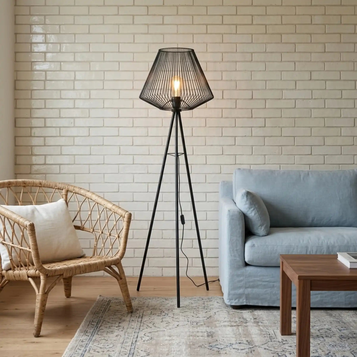 Lampadaire filaire noir devant un mur de briques blanches, entre un fauteuil en rotin et un canapé bleu clair