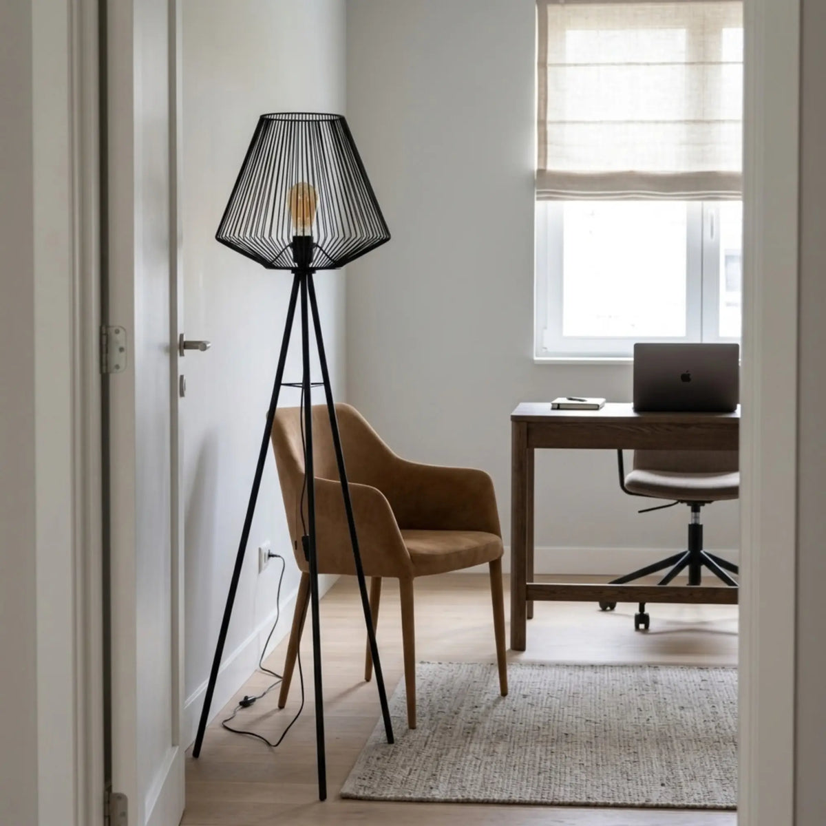 Lampadaire filaire noir allumé à l'entrée d'un bureau avec fauteuil en tissu, table de travail et ordinateur portable