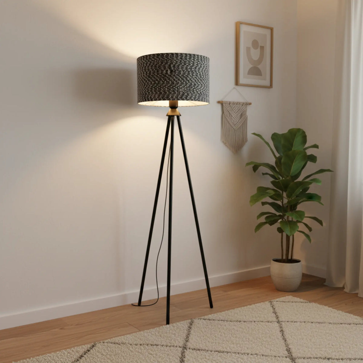 Lampadaire trépied allumé dans l'angle d'une pièce claire, à côté d'une plante verte et d'une suspension murale en macramé