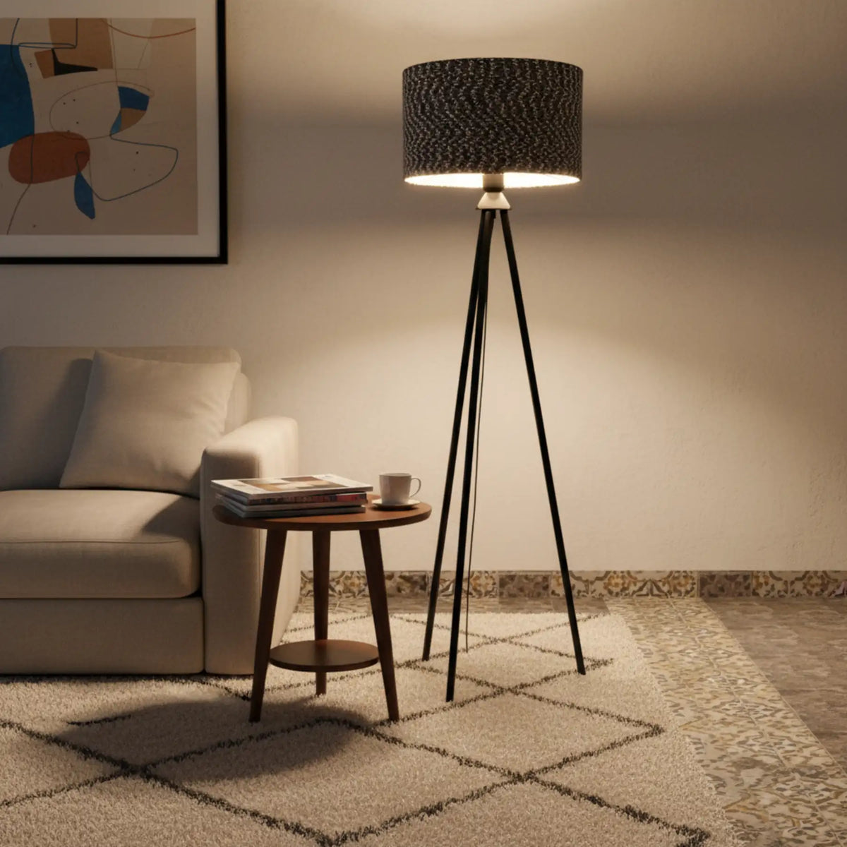 Lampadaire trépied noir allumé près d'un canapé beige et d'une table d'appoint ronde en bois, sur un tapis berbère
