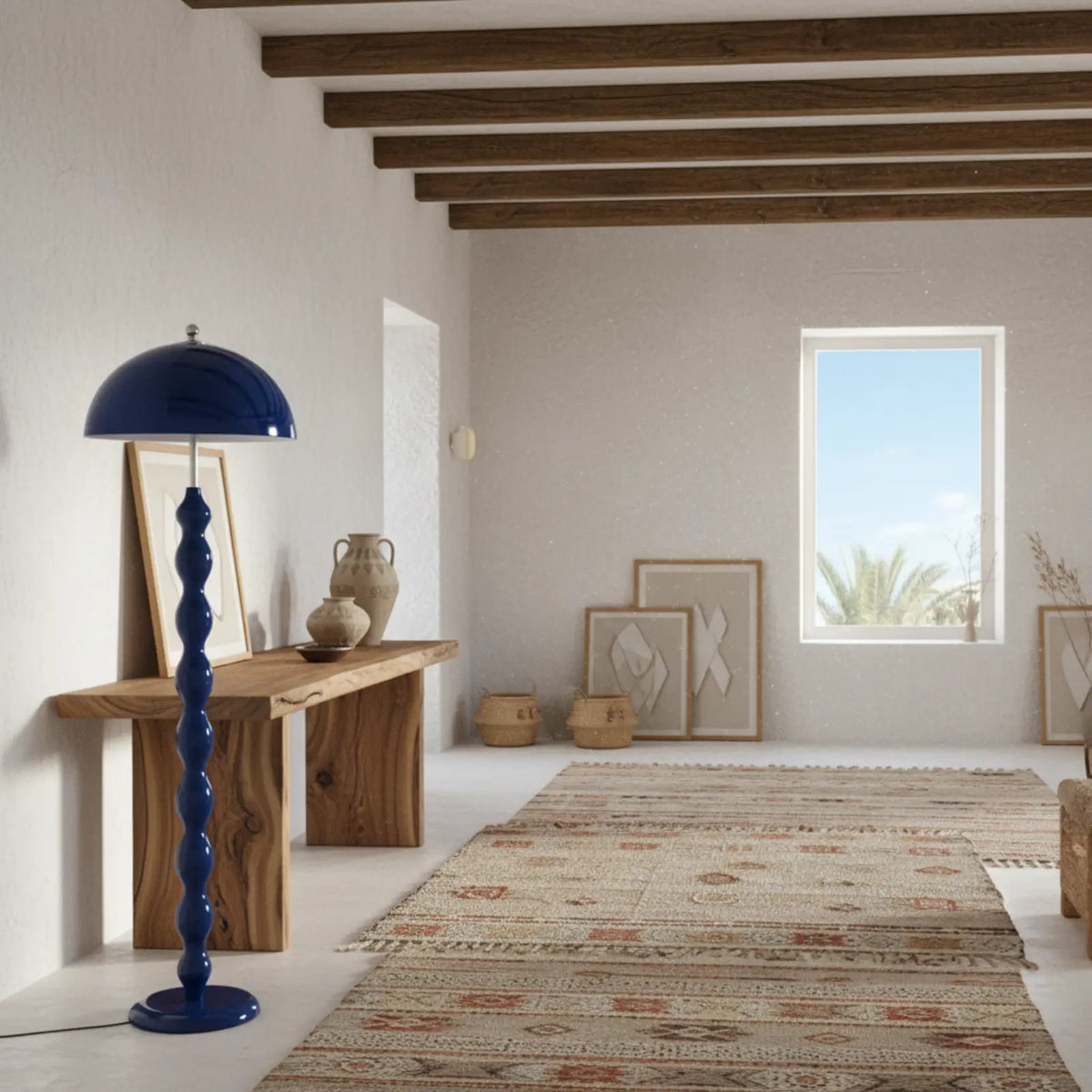 Lampadaire bleu près d'une console en bois massif, dans une pièce blanche aux poutres apparentes avec tapis kilim