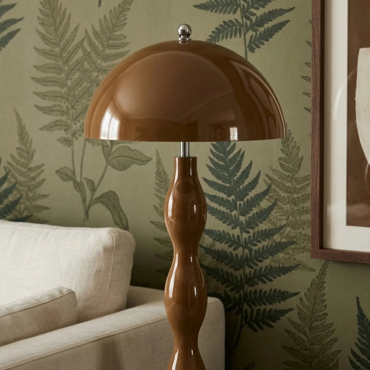 Lampadaire marron laqué devant un papier peint à motif fougères vert sauge, à côté d'un canapé blanc