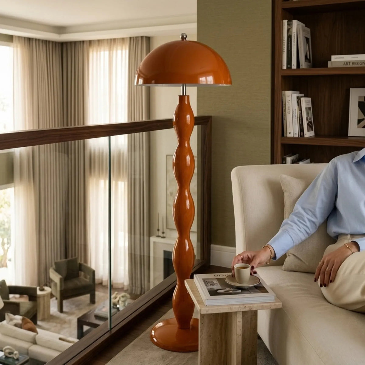 Lampadaire orange sur une mezzanine avec garde-corps en verre, à côté d'un canapé crème et d'une bibliothèque en bois