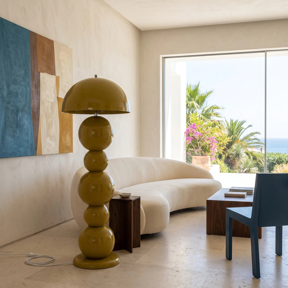 Lampadaire de salon vert olive à côté d'un canapé arrondi blanc, avec vue mer et palmiers