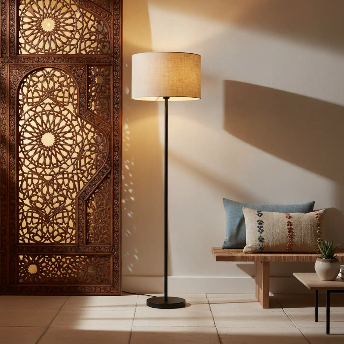 Lampadaire à abat-jour beige à côté d'un panneau moucharabieh en bois sculpté et d'une banquette avec coussins