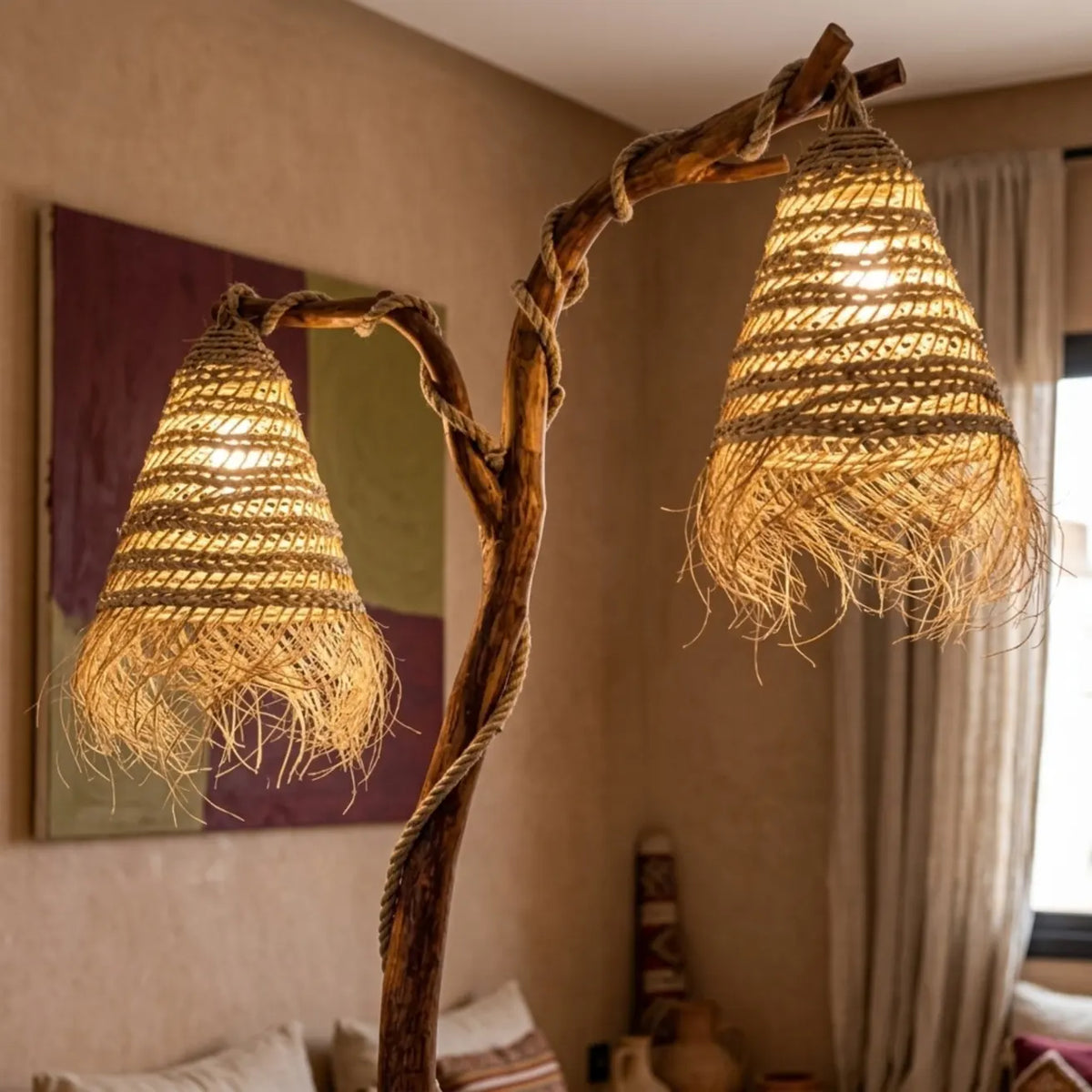 Gros plan sur les deux abat-jour à franges allumés, diffusant une lumière chaude depuis la branche de bois flotté