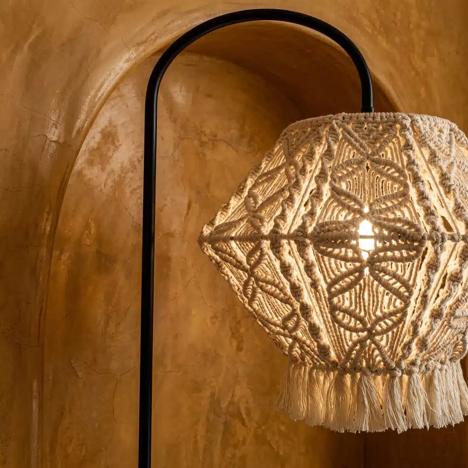 Abat-jour en macramé allumé laissant filtrer une lumière chaude, avec l'arc noir du lampadaire