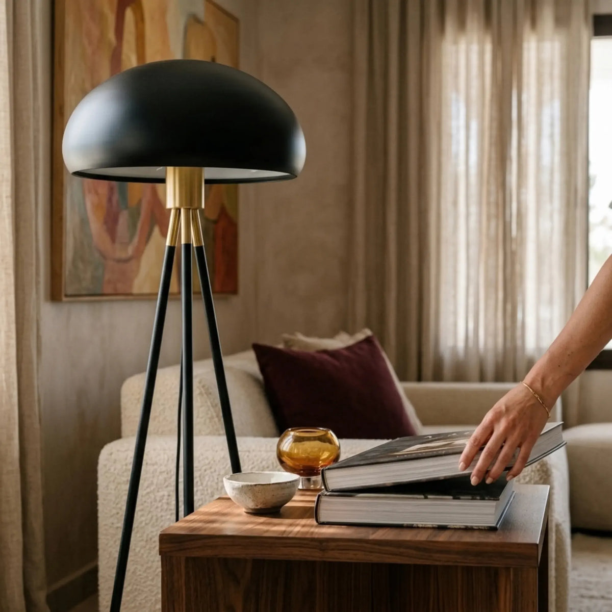 Gros plan sur l'abat-jour dôme noir et la bague dorée du lampadaire, à côté d'un canapé et d'une table d'appoint en bois