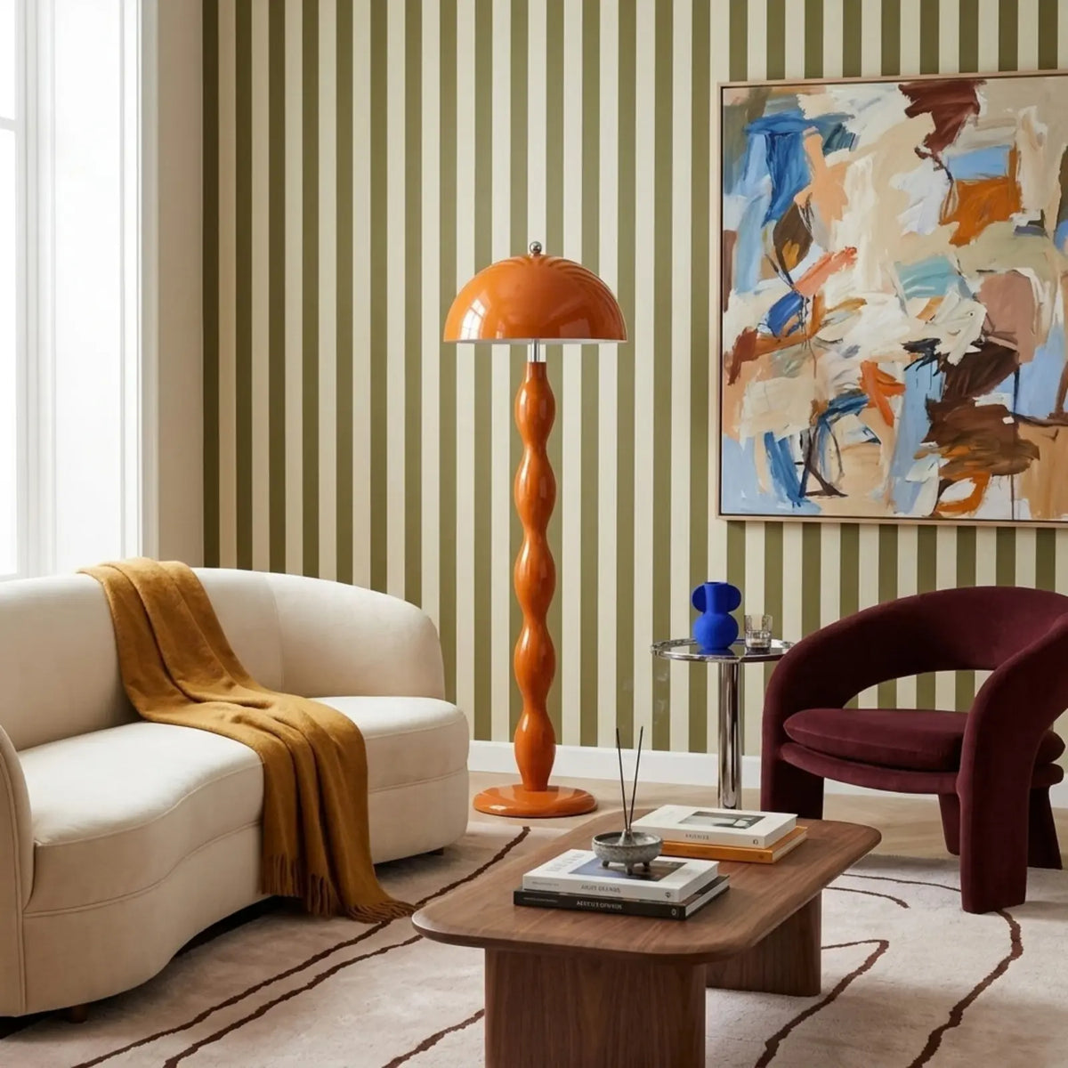Lampadaire orange dans un salon au papier peint rayé vert, entre un canapé arrondi crème et un fauteuil bordeaux