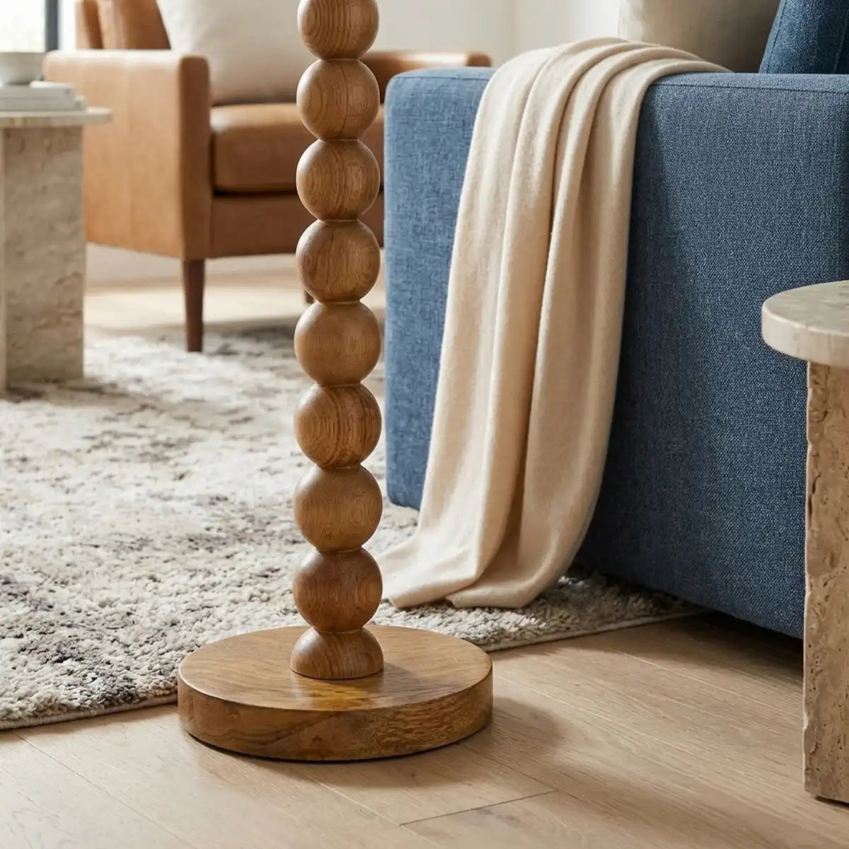 Détail des boules en bois rouge tourné et du socle rond du lampadaire, à côté d'un canapé bleu avec plaid crème