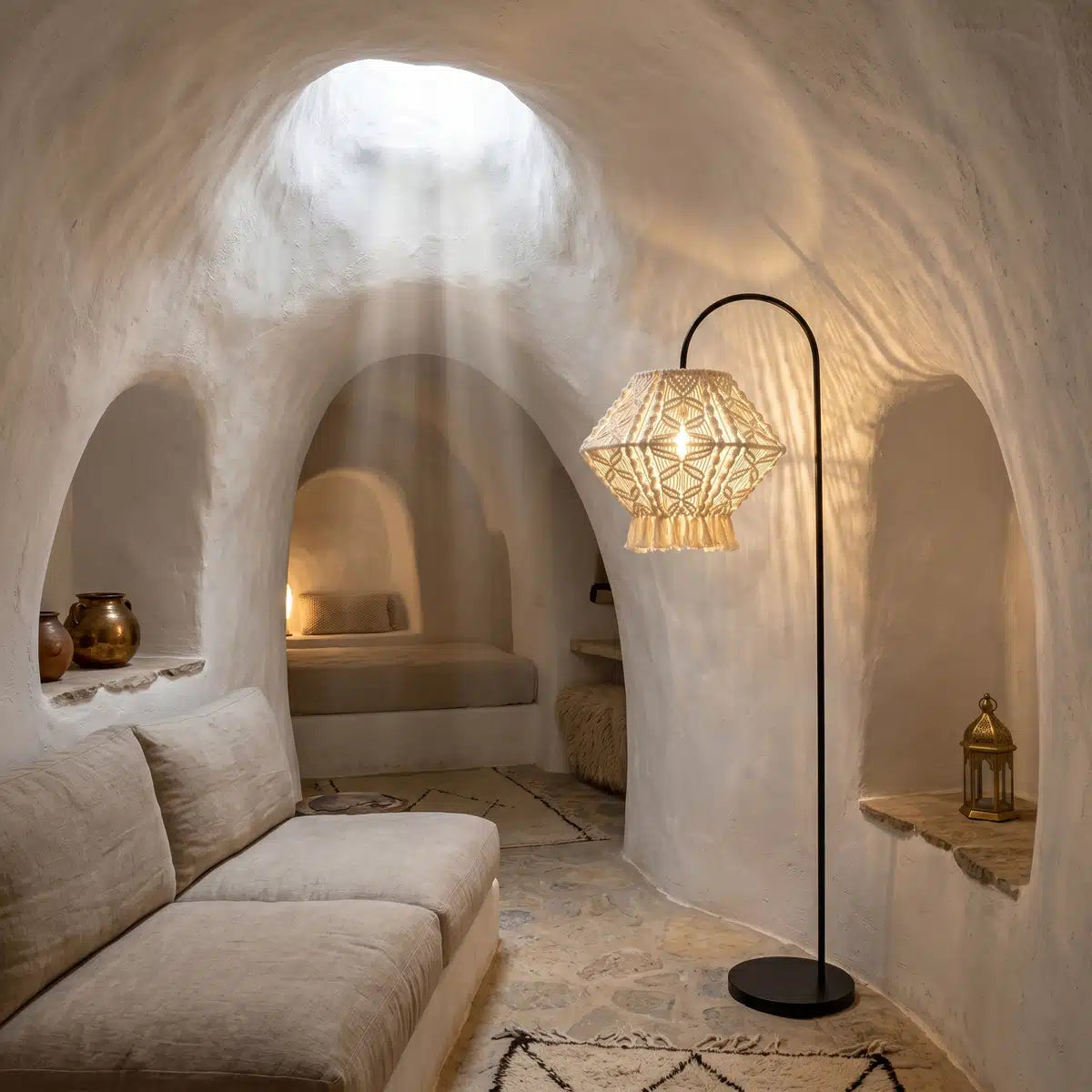 Lampadaire arc noir à abat-jour macramé dans un salon aux murs blancs arrondis, éclairé par une ouverture au plafond