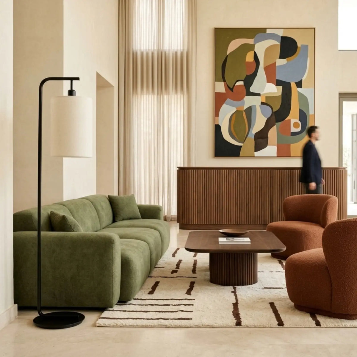 Lampadaire courbé noir au bout d'un canapé vert, face à des fauteuils rouille dans un grand salon