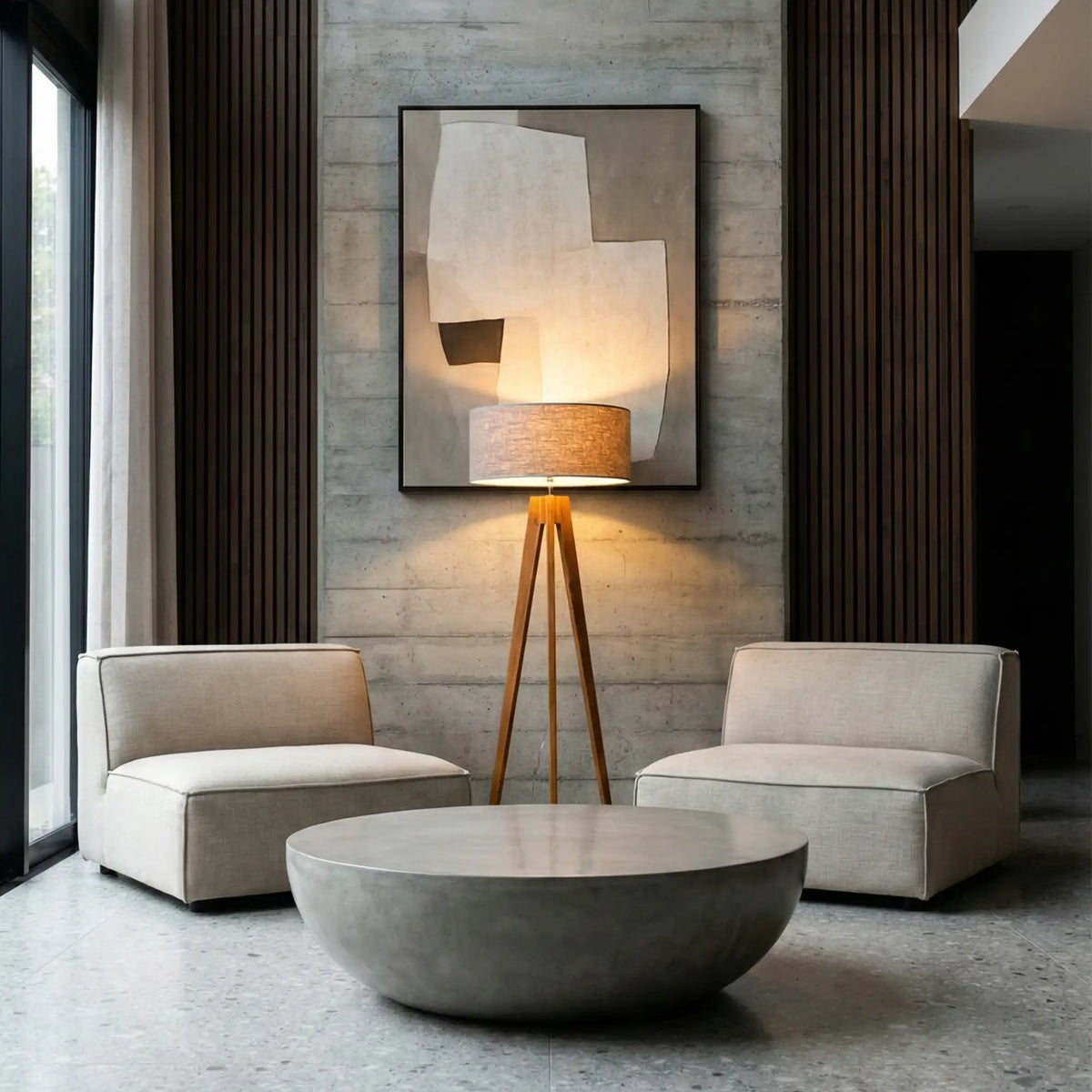 Lampadaire scandinave trépied allumé entre deux fauteuils crème, devant un tableau et une table basse ronde en béton