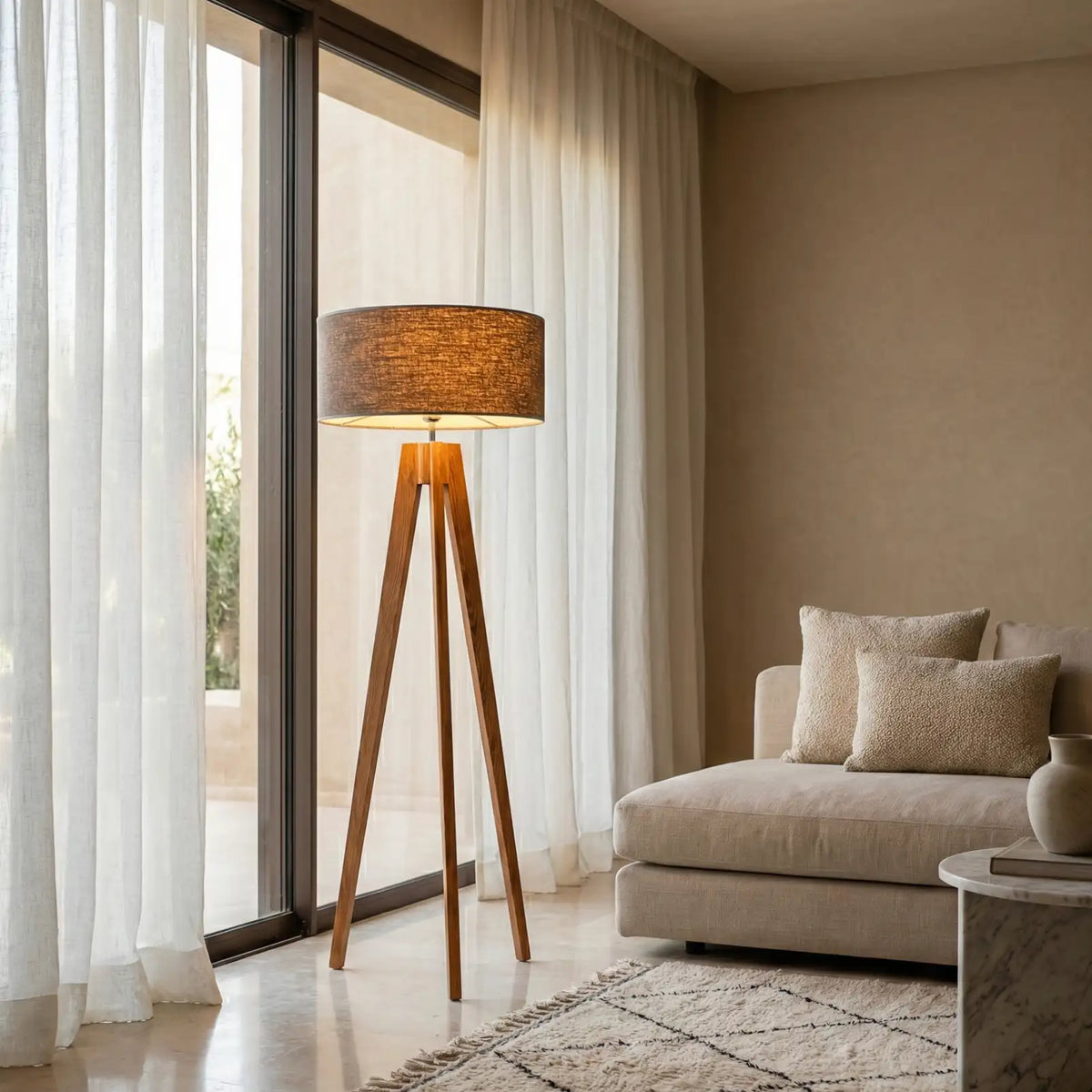 Lampadaire scandinave trépied près d'une baie vitrée aux voilages blancs, à côté d'un canapé beige