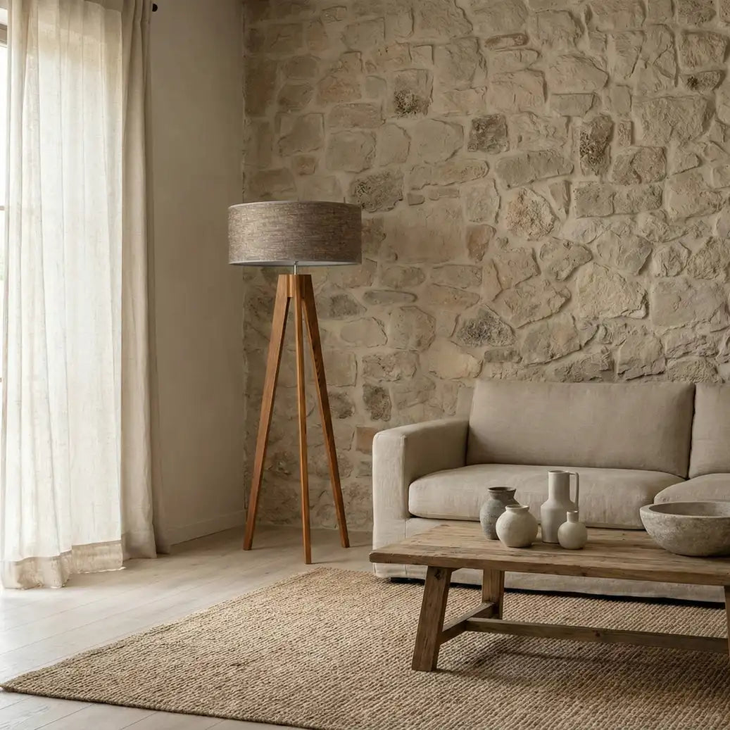 Lampadaire scandinave trépied devant un mur en pierre, à côté d'un canapé beige et d'une table basse en bois brut
