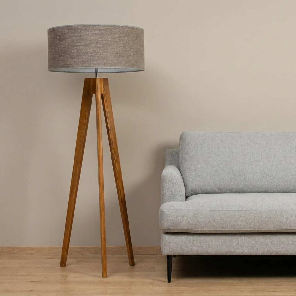 Lampadaire scandinave trépied en bois à côté d'un canapé gris clair, devant un mur beige