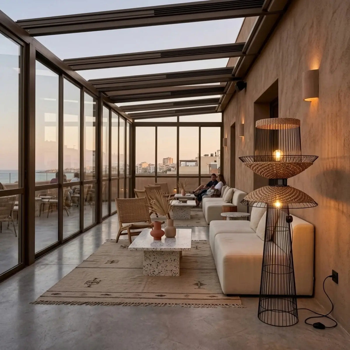 Lampadaire allumé sur une terrasse en véranda avec vue mer, à côté d'un canapé crème