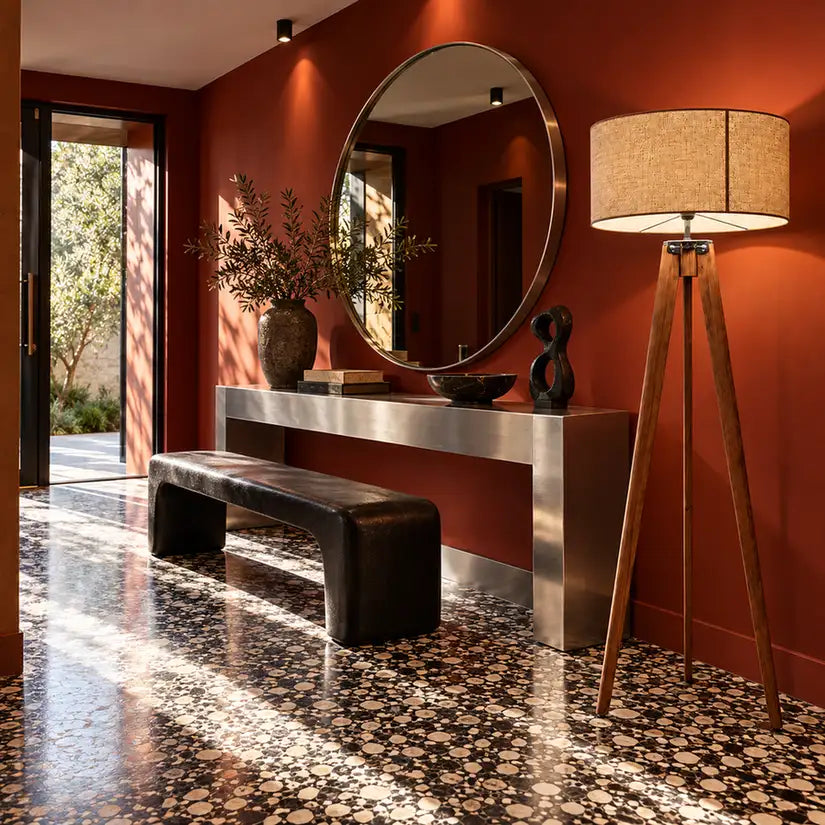 Lampadaire trépied en bois dans une entrée aux murs terracotta, à côté d'une console, d'un miroir rond et d'un sol en terrazzo