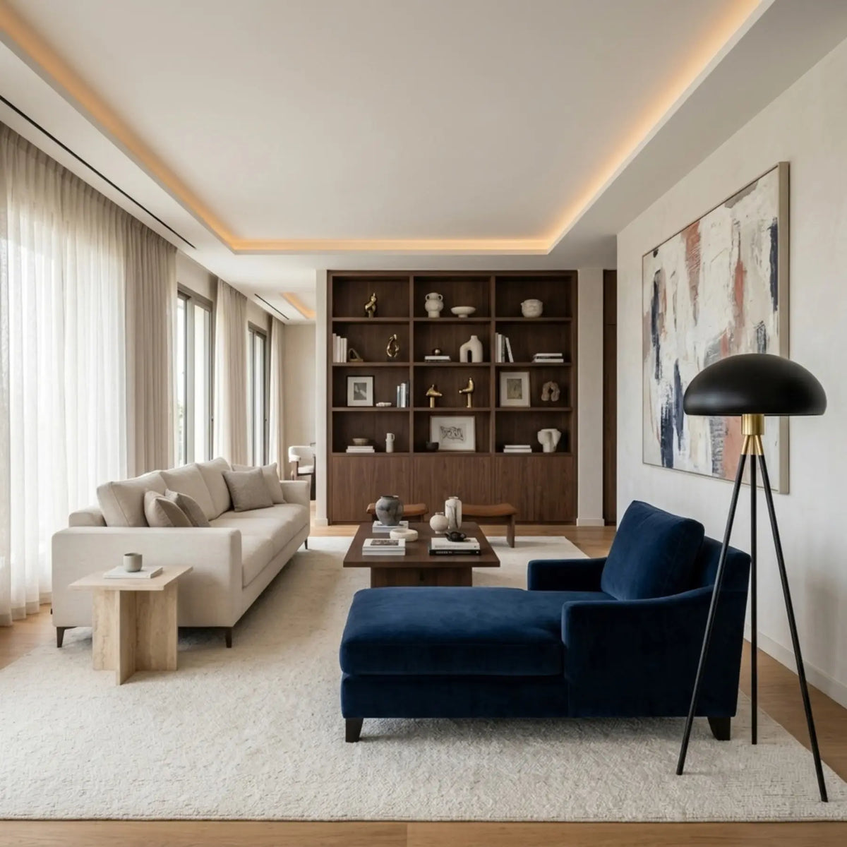 Lampadaire trépied noir près d'une méridienne bleu marine, dans un salon clair avec canapé crème et bibliothèque