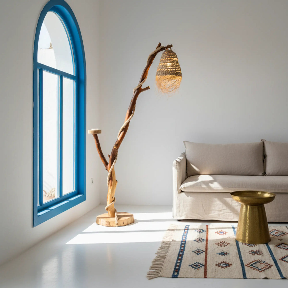Lampadaire bohème en bois flotté près d'une fenêtre cintrée bleue, d'un canapé beige et d'un tapis à motifs géométriques