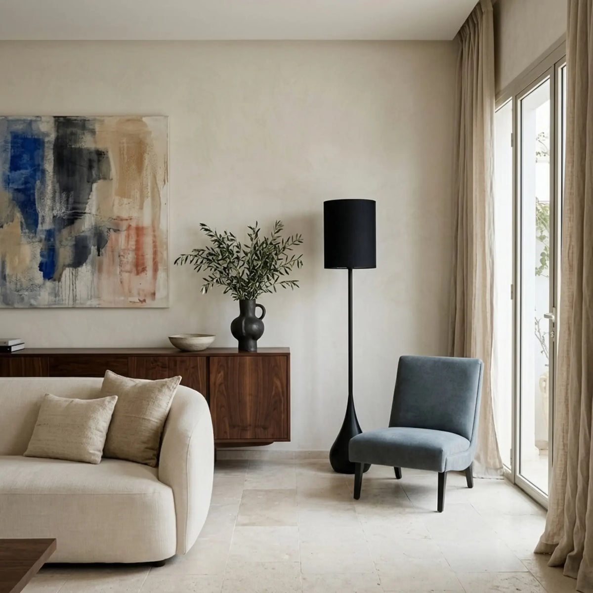 Lampadaire noir près d'un fauteuil gris-bleu et d'un canapé arrondi crème, dans un salon épuré aux murs clairs