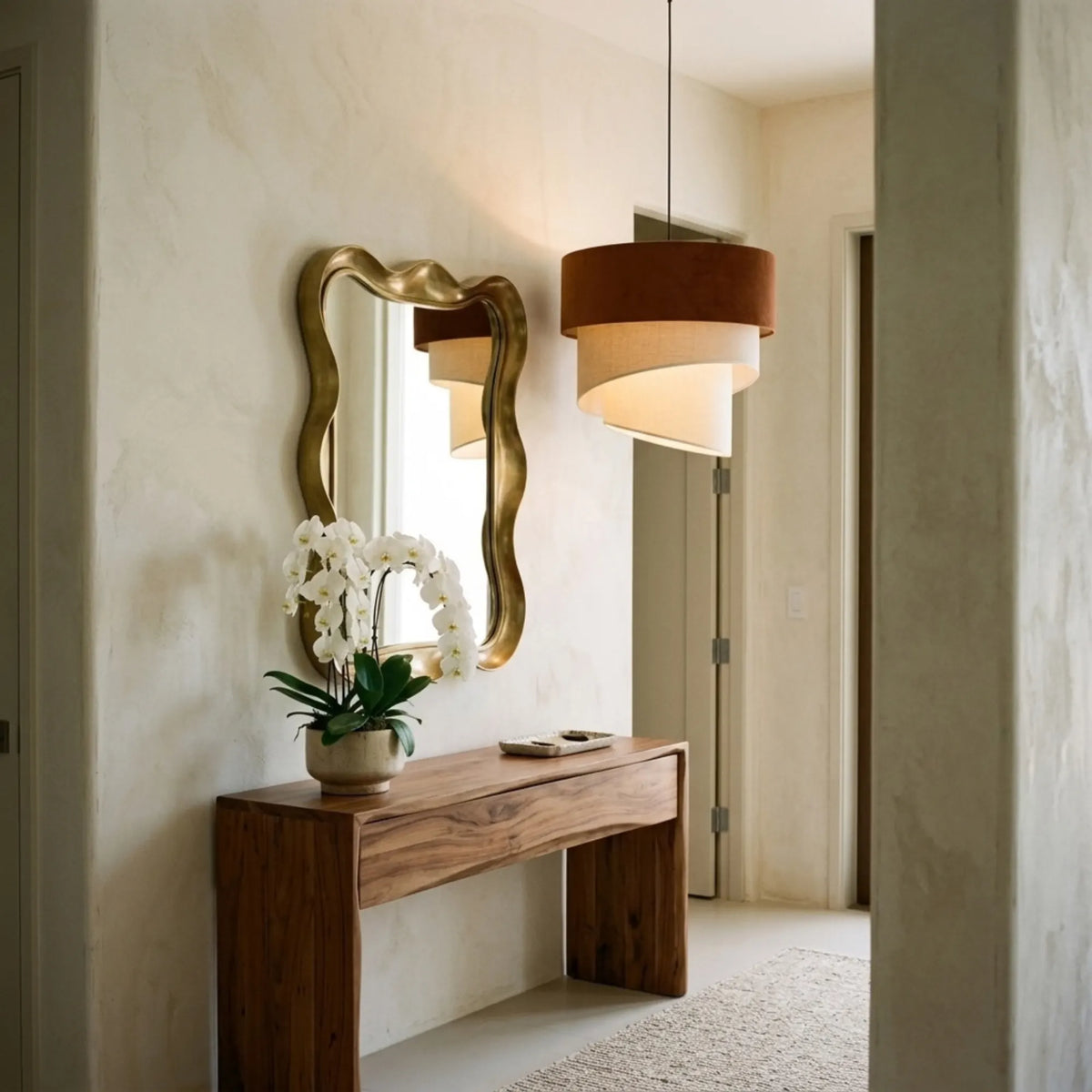 Lustre terracotta et crème dans une entrée avec console en bois et miroir ondulé doré