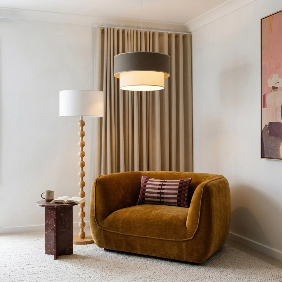 Suspension gris taupe allumée dans un salon avec fauteuil en velours moutarde et lampadaire sculpté