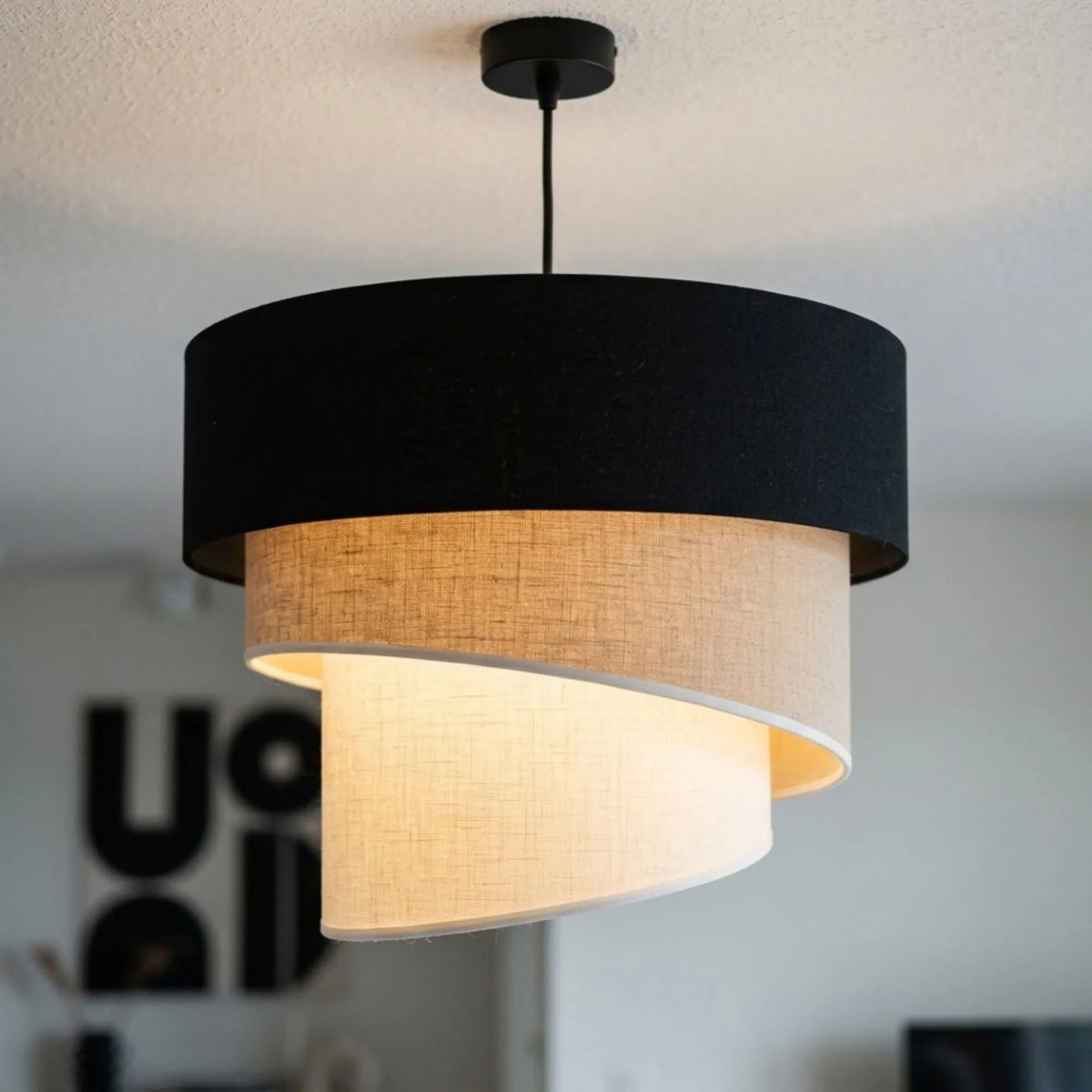 Gros plan sur la suspension trois tons allumée : tambour noir et volutes beige et crème texturées