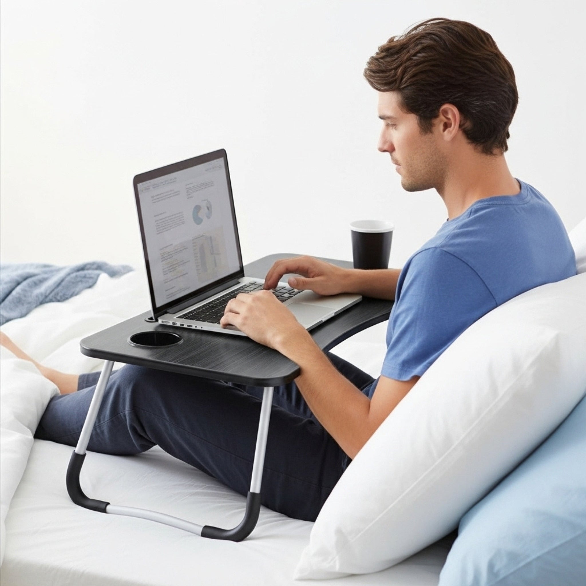 Un homme travaille sur son ordinateur portable avec une table de lit pliante noire, parfaite pour le télétravail en Tunisie