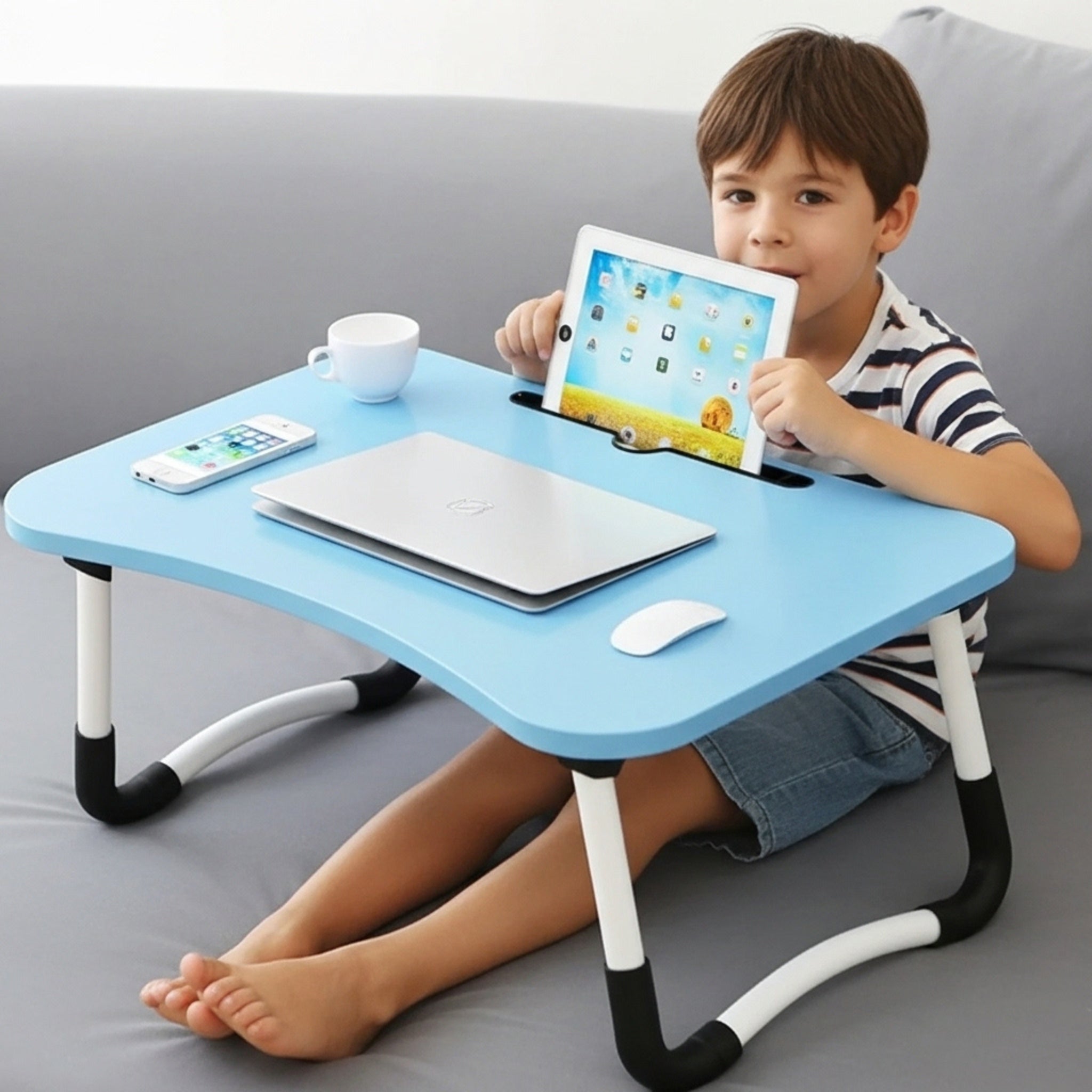 Un jeune garçon utilise une table de lit pliante bleue pour sa tablette et son ordinateur, un accessoire idéal pour les enfants en Tunisie.