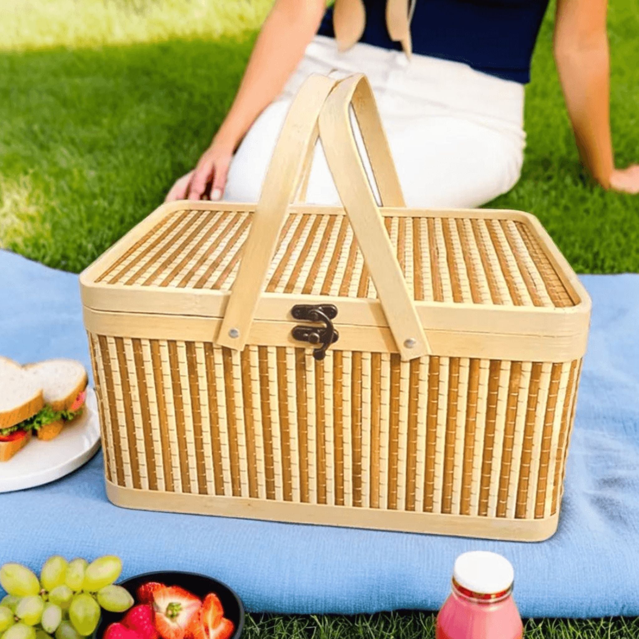 Une femme assise sur l'herbe avec un panier de pique-nique en bambou tressé sur une couverture bleue.