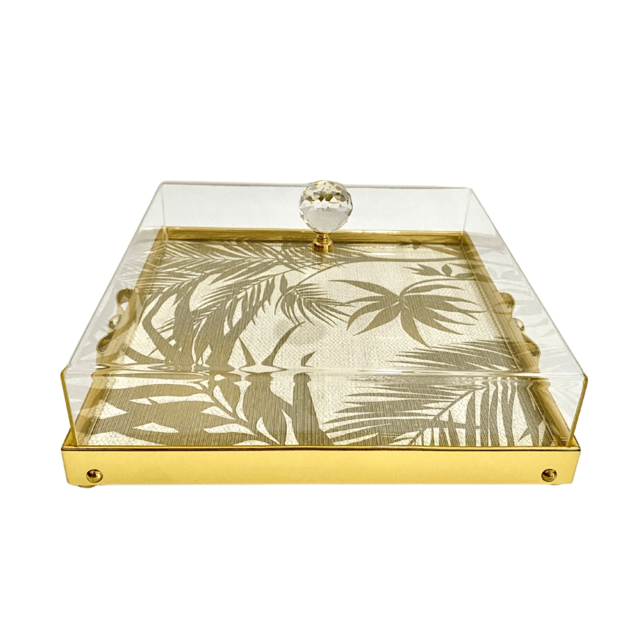 Plateau doré avec couvercle transparent, poignée en cristal, et motif de feuilles tropicales. Idéal pour présenter gâteaux et desserts.