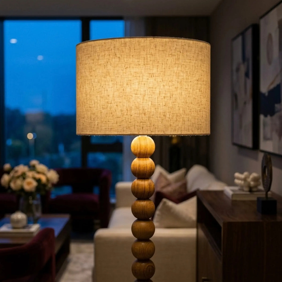 Abat-jour en lin allumé et boules en bois rouge du lampadaire, dans un salon le soir devant une baie vitrée