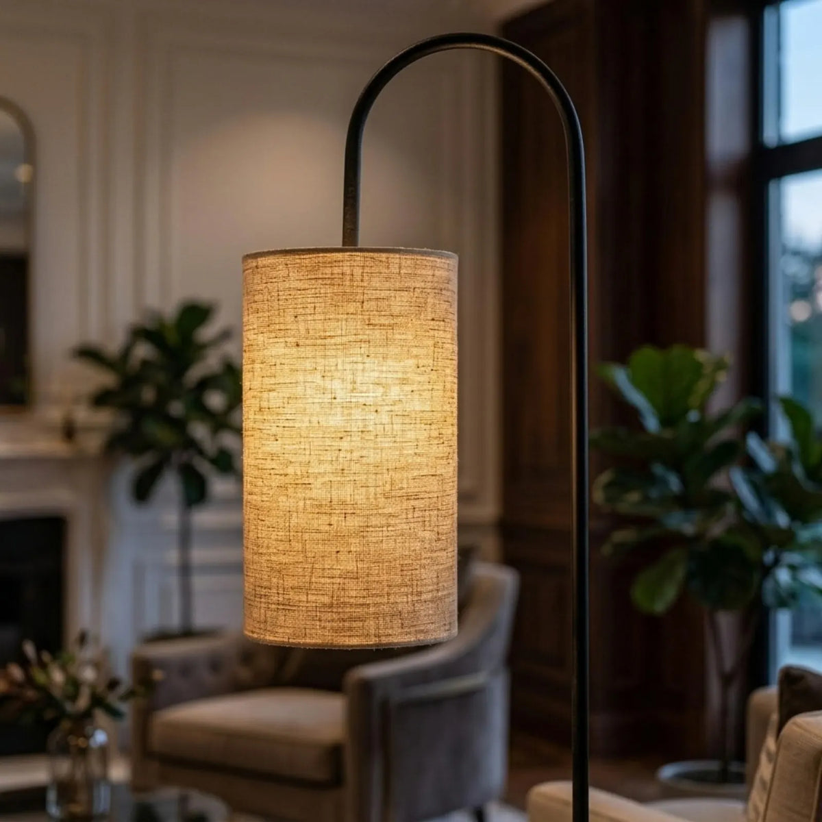 Abat-jour cylindrique en lin beige allumé au bout du bras noir du lampadaire
