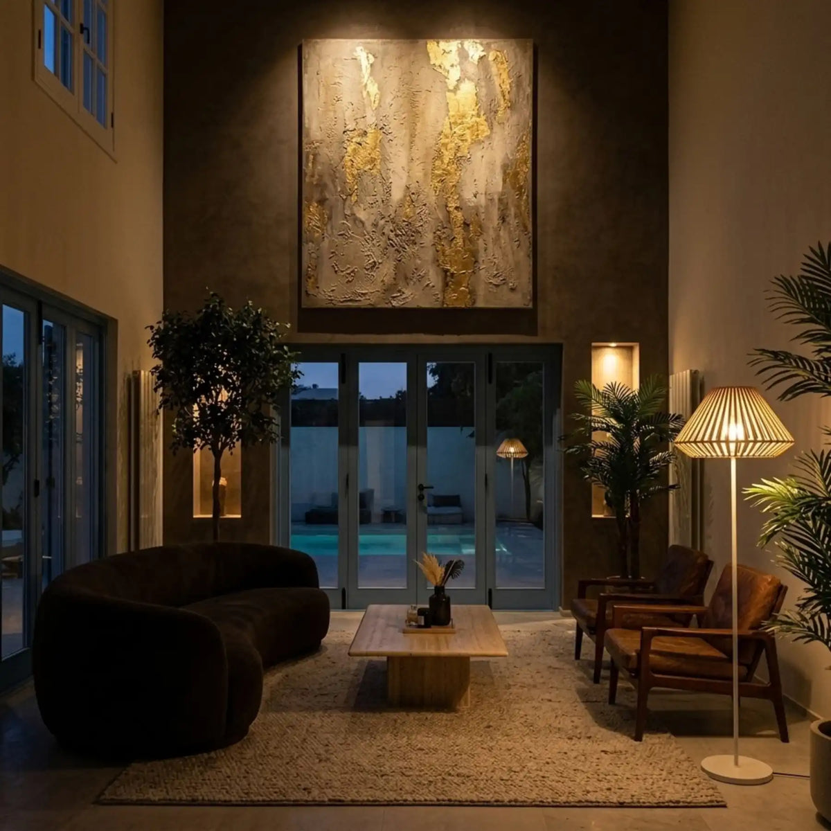 Lampadaire allumé de nuit dans un salon ouvert sur la piscine, près d'un fauteuil en bois et d'un canapé noir