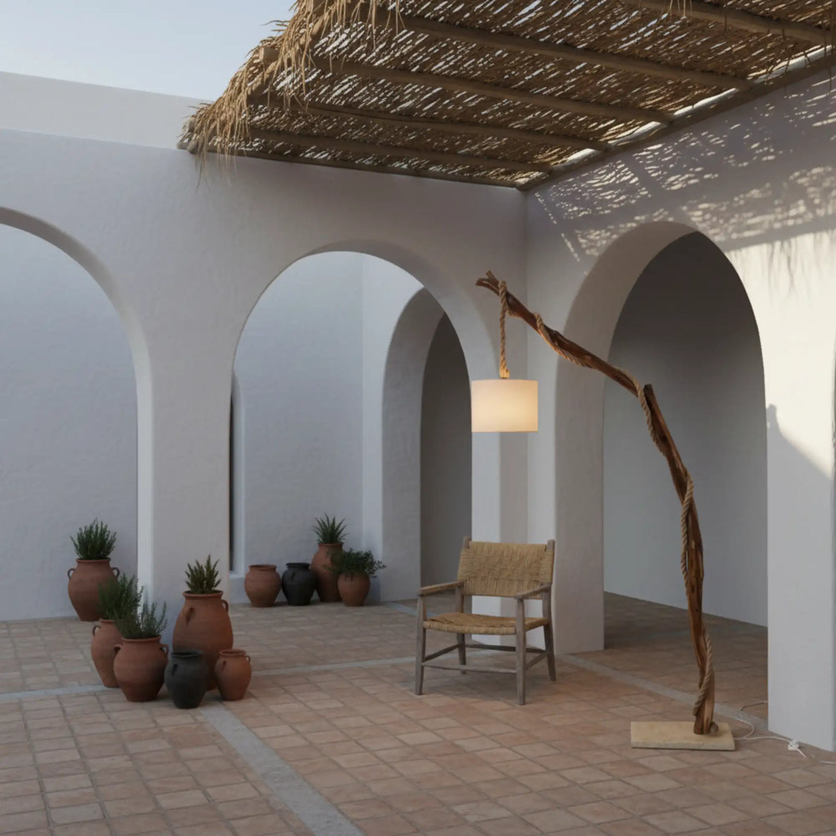 Lampadaire en bois naturel sous une pergola en roseau, dans un patio à arcades blanches avec pots en terre cuite